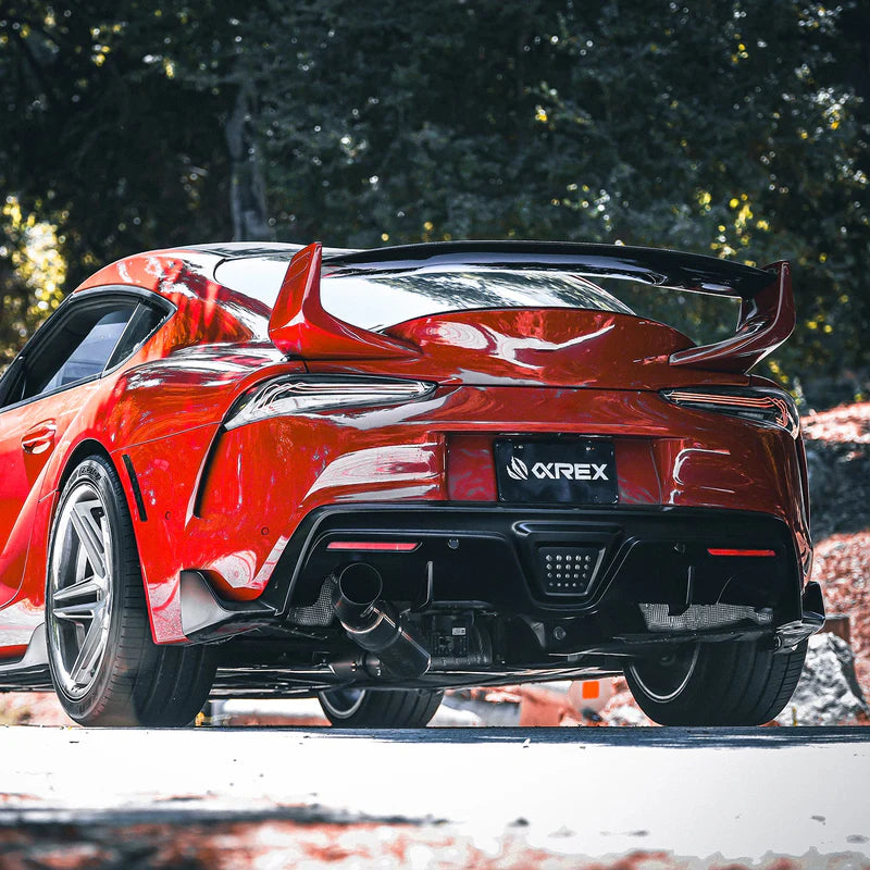 Red sports car with a visible brand logo on a blurred natural background